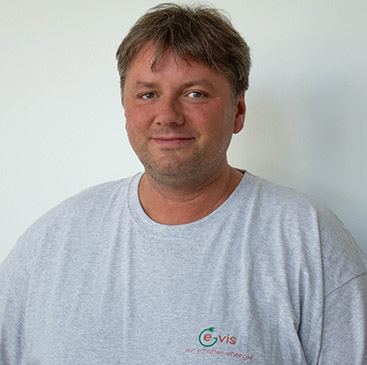 Eine lächelnde Person mit grauem T-Shirt vor weißem Hintergrund.