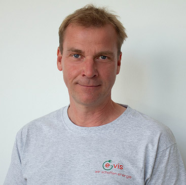 Mann mit freundlichem Ausdruck, graues T-Shirt, kurzes hellbraunes Haar.